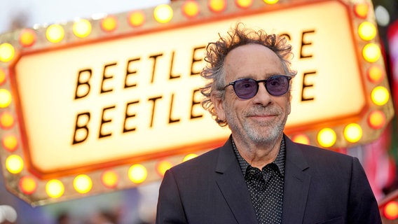 Ein Mann mit dunkler Brille lächelt von einem Neon-Schild zum Film "Beetlejuice, Beetlejuice" © Foto: Yui Mok/PA Wire/dpa +++ dpa-Bildfunk +++ Foto: Yui Mok