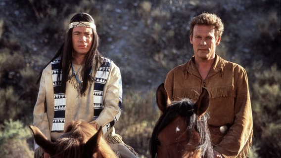 Zwei Männer, verkleidet als Indigene, reiten auf Pferden © picture alliance/United Archives 