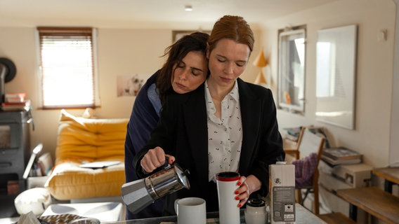 Die Schauspielerin Karolin Herfurth schenkt Kaffee in eine Tasse, während sich die Schauspielerin Nora Tschirner an sie lehnt. © 2024 Hellinger / Doll Filmproduktion GmbH / Warner Bros. Entertainment GmbH Foto:  Anne Wilk