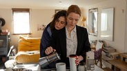 Die Schauspielerin Karolin Herfurth schenkt Kaffee in eine Tasse, während sich die Schauspielerin Nora Tschirner an sie lehnt. © 2024 Hellinger / Doll Filmproduktion GmbH / Warner Bros. Entertainment GmbH Foto:  Anne Wilk