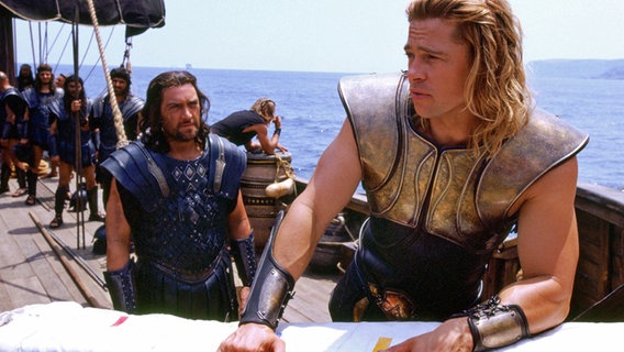 Szenenbild aus "Troja": Achilles (Brad Pitt) steht auf einem Segelschiff, hinter ihm sieht man die Mannschaft. © picture alliance/United Archives | United Archives/Impress 