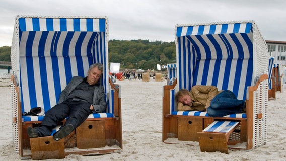 Henry Hübchen und Markus Hering liegen in einer Szene des Films "Whisky mit Wodka" in nebeneinander stehenden Strandkörben an einem Strand © Filmland MV 