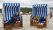 Henry Hübchen und Markus Hering liegen in einer Szene des Films "Whisky mit Wodka" in nebeneinander stehenden Strandkörben an einem Strand © Filmland MV 