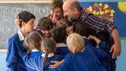 Szene aus dem Film "Willkommen in den Bergen": Ein Mann, eine Frau und Schülerinnen und Schüler umarmen sich. © Claudio Iannone / Filmwelt 