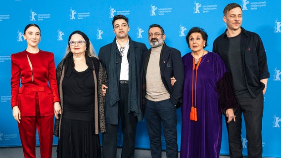 Eine Gruppe von Männern und von Frauen, eine davon deutlich älter, steht vor einer blauen Wand bei einem Filmfest © Berlinale 2025 / Dirk Michael Deckbar Foto: Dirk Michael Deckbar