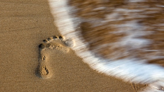 Ein Fußabdruck am Strand wird von einer Welle überspült © picture alliance / photothek Foto: Thomas Trutschel