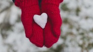 Rote Handschuhe halten ein Stoffherz in den Händen. © picture alliance / Zoonar | Oleksandr Latkun Foto: Oleksandr Latkun