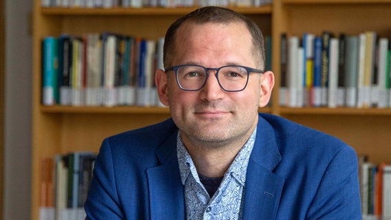 Florian Höhne sitzt vor einer Bücherwand und blickt in die Kamera. © Georg Pöhlein 