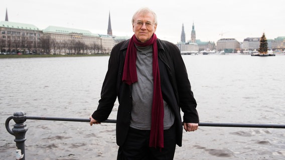 Ein Mann steht an einem Geländer an der Hamburger Alster, im Hintergrund sind Häuser und Türme der Stadt Hamburg zu sehen © picture alliance / dpa | Daniel Bockwoldt 