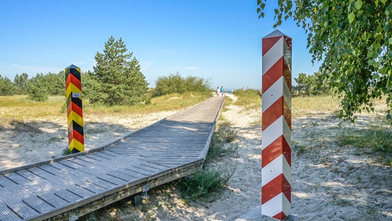 Ein Bohlenweg vom Strand in Richtung Land führt zwischen Grenzpfosten durch, die mit den Farben der deutschen und der polnischen Flagge bemalt sind. © picture alliance Foto: imageBROKER  Schoening