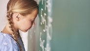 Ein Mädchen lehnt ihren Kopf an eine Tafel. Ihre Augen sind geschlossen. © fotolia.com Foto: gpointstudio