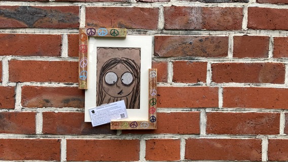 Eine Zeichnung von einem schielenden Mädchen hängt in einem Rahmen an einer Mauer. © NDR Foto: Antonia Reiff