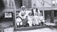 Ein Mann sitzt mit seiner Frau und sechs Kindern auf einer Stufe von einer Holztreppe. © South Australian Museum, Adelaide Foto: Edgar Ravenswood Waite