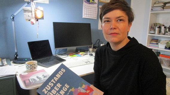 Karen Obenauf sitzt an ihrem Schreibtisch und hält ein Buch in der Hand © NDR.de Foto: Axel Seitz