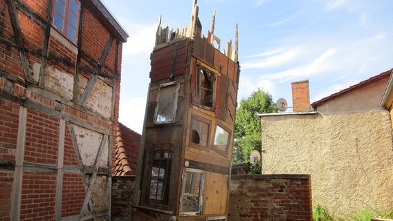 Ein schiefer Turm aus Holz in einem Innenhof von Fachwerkhäusern. © NDR Foto: Axel Seitz