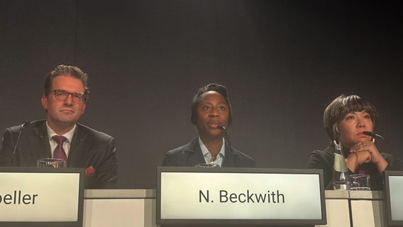 Hinter einem breiten Podium, auf dem drei Namen stehen, ist in der Mitte eine Frau, auf ihrem Namensschild steht Naomi Beckwith. © picture alliance/dpa | Nicole Schippers Foto: Nicole Schippers