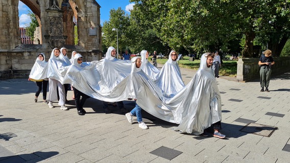 Menschen mit silbernen Kapuzen gehen bei den Kulturdreieck Festwochen über einen Platz © NDR.de Foto: Agnes Bührig