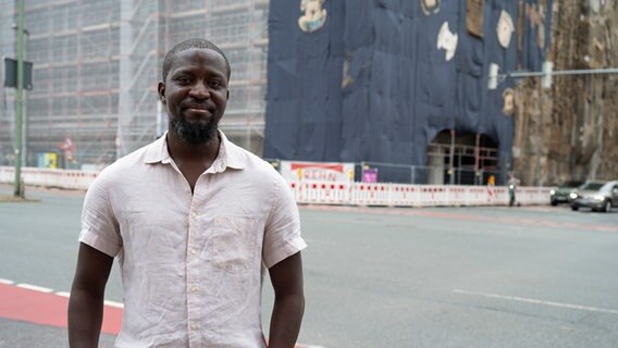 Künstler Ibrahim Mahama steht vor einem mit Jutesäcken verhüllten Kaufhaus in Osnabrück © Kunsthalle Osnabrück 