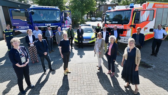 Museums- und ArchivmitarbeiterInnen stehen auf einem Platz und schauen in die Kamera. Im Hintergrund ein Lkw des THW, ein Polizeiwagen und ein Feuerwehrwagen. © Landesmuseum Natur und Mensch Oldenburg Foto: Torsten von Reeken