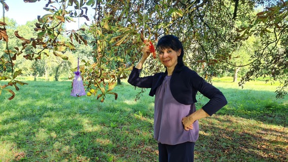 Die Künstlerin Natalie Deseke hält ein orangefarbenes Stoffbeutelchen, dass mit einem Seil an einem Baum befestigt ist. © NDR Foto: Agnes Bührig