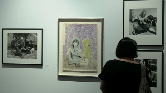 Eine Besucherin der Galerie im Marstall in Ahrensburg steht vor Grafiken von Pablo Picasso und einem Foto von ihm. © NDR 