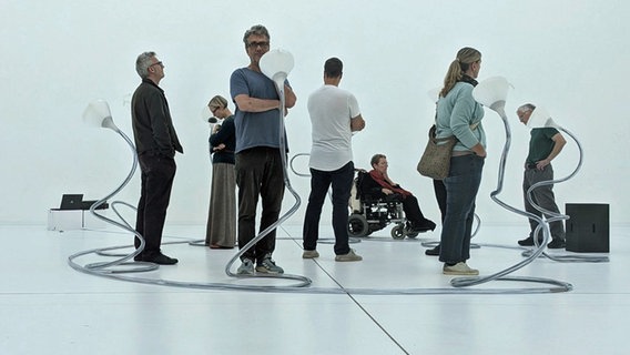 Einige Personen stehen in einem weißen Raum zwischen Ausstellungsstücken. Es ist der Künstler Peter Tucholski und das Team der Alzheimer Gesellschaft M-V. © NDR 