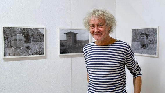 Ein Mann mit grauen Haaren steht lächelnd vor einer Wand mit Schwarz-Weiß-Fotos von Jagdhochsitzen (Stefan Nestler) © NDR Foto: Peter Scherrer