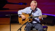 Wolf Biermann sitzt mit seiner Gitarre auf der Bühne der Elbphilharmonie. © Georg Wendt/dpa 