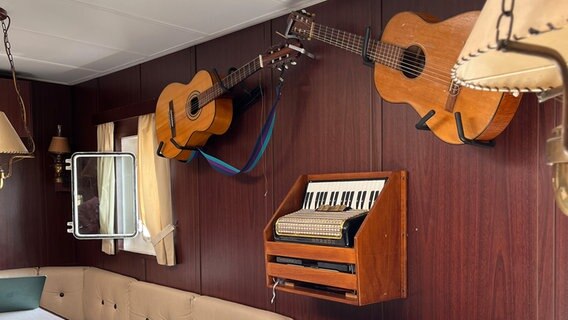 Zwei Gitarren hängen an der Wand der Schiffsmesse. Zwischen den Gitarren hängt ein altes Akkordeon. © NDR Foto: Tom Holste