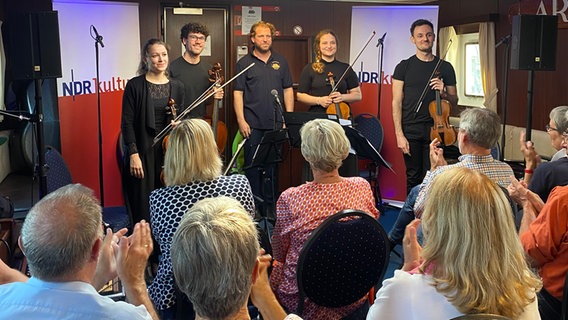 Das Ensemble steht mit Julian Prégardien in ihrer Mitte und lächelt. Die Zuhörenden applaudieren. © NDR Foto: Tom Holste