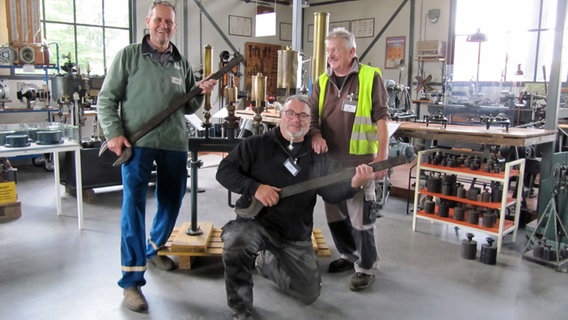 Drei Männer posieren vor technischen Geräten; zwei von ihnen halten riesige Schrauneschlüssel wie Gitarren in der Hand. © NDR Foto: Jens Zacharias