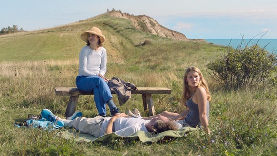 Eine dreiköpfige Familie sitzt und liegt auf einer Wiese. © Adomeit Films 