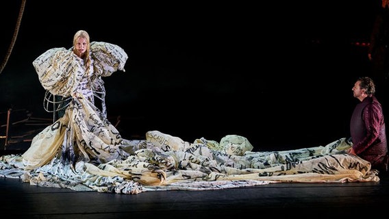 Szenenbild: Eine Frau in einer großen Robe mit langer Schleppe singt auf einer Bühne. © Enrico Nawrath/Bayreuther Festspiele 