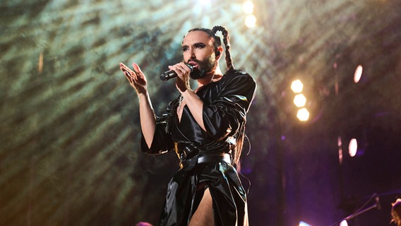 Die Musikerin Conchita Wurst mit Zöpfen und dunkler Lederkleidung singt auf der Bühne © Annette Riedl/dpa +++ dpa-Bildfunk +++ Foto: Annette Riedl