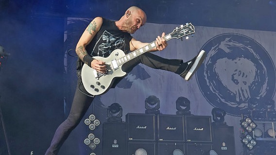 Der Gitarrist der Band Rise Against, Zach Blair, springt mit der Gitarre in der Hand auf einer Bühne © picture alliance / Thomas Frey/dpa | Foto: Thomas Frey