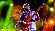 Der Bassist Richard Bona spielt auf einer bunt beleuchteten Bühne Bass und singt in ein Mikrofon. © picture alliance / Godong Foto: Philippe Lissac