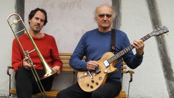 Der Posaunist Nils Wogram und Gitarrist Joe Sachse sitzen mit ihren Instrumenten auf einer Bank. © Corinne Hächler Foto: Corinne Hächler