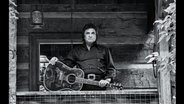 Auf einem schwarz-weiß-Bild steht ein Mann auf seiner Veranda mit seiner Gitarre (Johnny Cash auf den Cover seines posthum erschienen Album "Songwriter") © Universal Music/dpa 