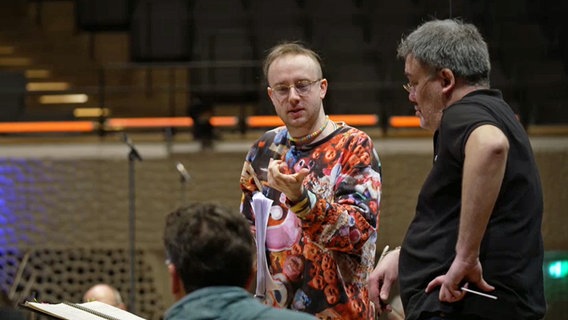 Alex Paxton im Gespräch mit Musikern im Orchester © NDR.de 