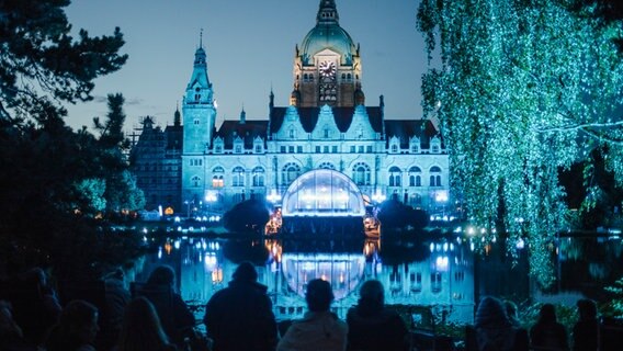 Besucher des NDR Klassik Open Air sitzen im Maschpark mit Blick auf das blau erleuchtete Rathaus. © NDR Foto: Julius Matuschik