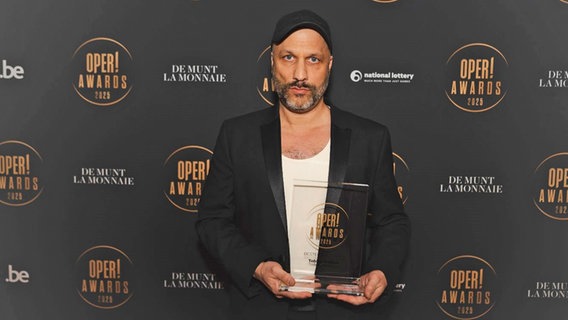 Ein Mann mit Käppi hält eine Trophäe in der Hand bei einem Pressetermin - der Regisseur und künftige Opernintendant an der Staatsoper Hamburg Tobias Kratzer © Simon Van Rompay Foto: Simon Van Rompay