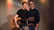 Zwei Männer stehen nebeneinander. Einer hält eine Gitarre mit zwei Hälsen in der Hand. © Franziska Dieckmann / NDR Foto: Franziska Dieckmann / NDR