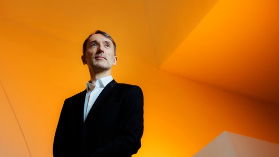 Olivier Latry steht vor einem orangenen Hintergrund © William Beaucardet 