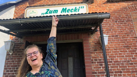 Eine Frau (Jane Thorun) zeigt mit dem Finger auf den Namenszug des Lokals "Mecki" in Hagenow. © NDR.de Foto: Axel Seitz