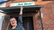 Eine Frau (Jane Thorun) zeigt mit dem Finger auf den Namenszug des Lokals "Mecki" in Hagenow. © NDR.de Foto: Axel Seitz