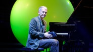 Ein Mann mit grauen kurzen Haaren sitzt am schwarzen Flügel und schaut ins Publikum, dahinter leuchtet es grün (Jazzpianist Brad Mehldau) © imago images/Sven Thielmann Foto: Sven Thielmann