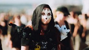 Ein Mann mit einer weißen Maske, Kapuze und schwarzer Kleidung läuft auf dem Festival M'era Luna 2023 herum © M'era Luna 2023 /  Christoph Eisenmenger Foto: Christoph Eisenmenger