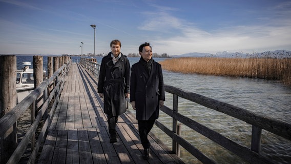 Nils Mönkemeyer und William Youn spazieren auf einer Brücke umgeben von einer winterlichen Landschaft © Irène Zandel 