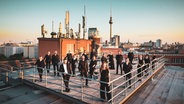 Eine Gruppe von Menschen steht auf einem Dach, im Hintergrund der Berliner Fernsehturm © Simon Hertling 