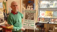 Ein Mann hält ein Plakat mit einem Konzerthinweis zu Littler Richard und den Beatles in die Kamera © NDR.de Foto: Ocke Bandixen